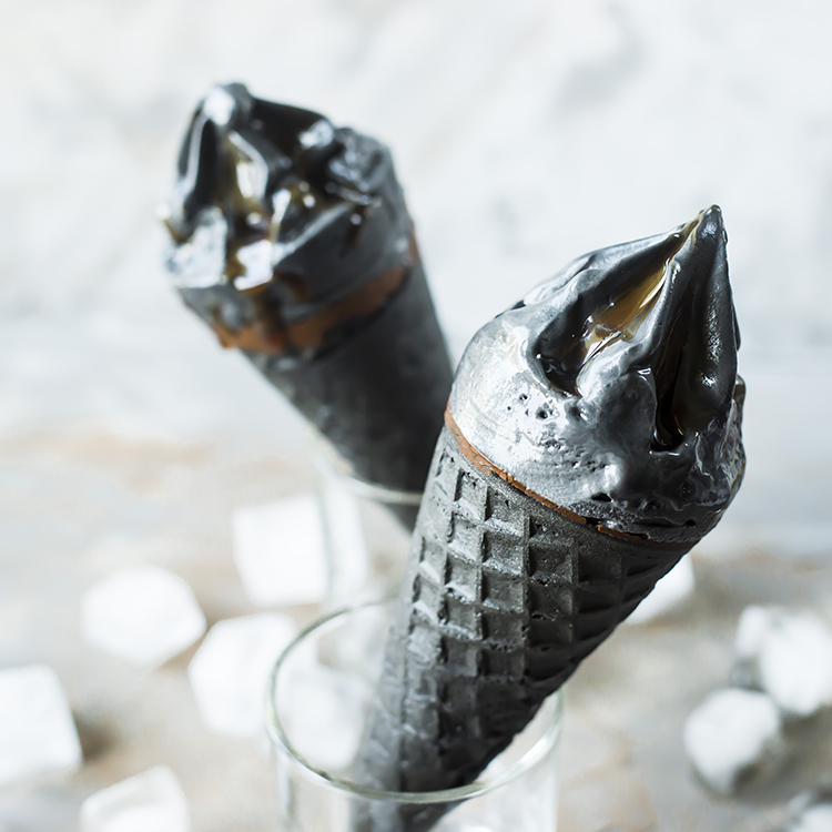 Two black ice cream in waffle cones on a gray background. Summer trend dessert