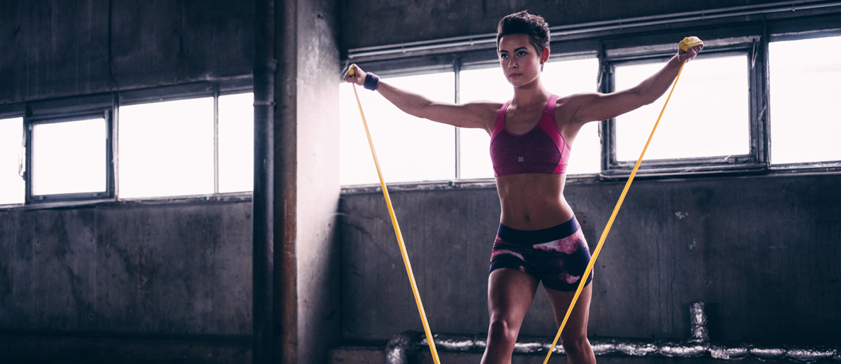 junge frau traniert mit einem gelben fitnessband im studio