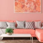 große couch mit hocker in der trendfarbe living coral vor einer wand in living coral mit einem wandbild im bilderrahmen