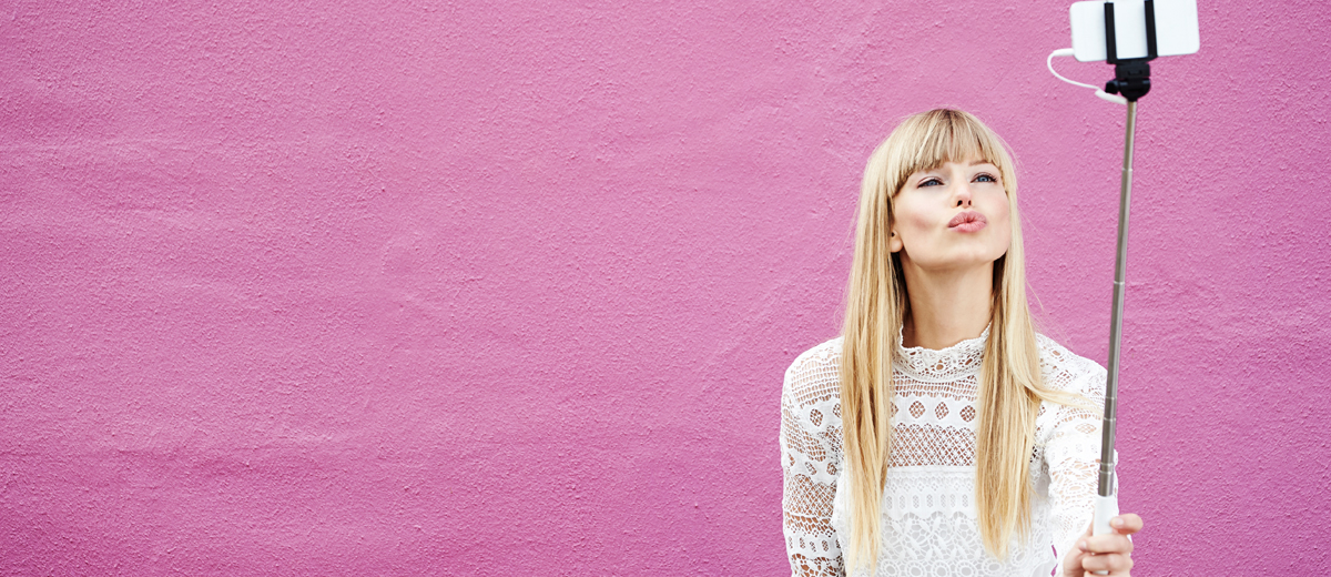 junge frau posiert vor pinkfarbener Wand mit selfie-stick