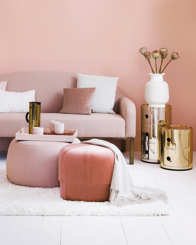 ausschnitt aus einem wohnzimmer mit sofa und hocker in living coral und rose. daneben beistelltische in gold