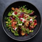 schale mit salat aus quinoa, rüben, spinat und granatapfelkernen auf einem dunklen untergrund