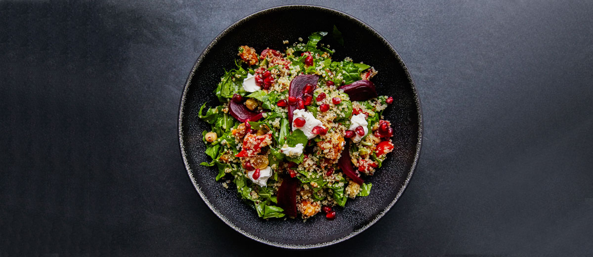 schale mit salat aus quinoa, rüben, spinat und granatapfelkernen auf einem dunklen untergrund