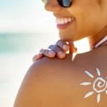 junge frau am strand mit sonnencreme auf dem rücken