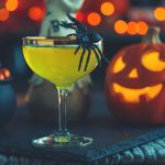 cocktailglas mit einer spinne vor einer halloween deko stehend