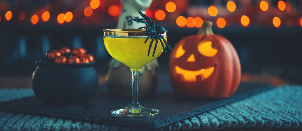 cocktailglas mit einer spinne vor einer halloween deko stehend