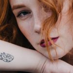 junge frau mit roten haaren und kleinem tattoo auf dem arm