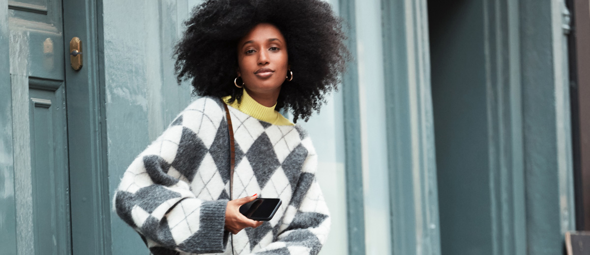 Frau mit Afrolocken trägt Trend-Pullover mit Argyle-Muster