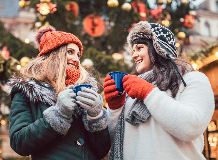 Zwei Freundinnen trinken draußen im Winter warme Getränke