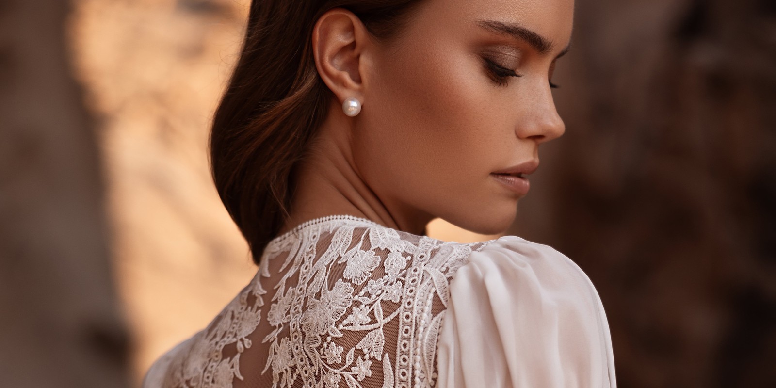 Nahaufnahme des Brautkleids Etra von DAMA Couture mit floraler Spitze am Rücken und einem Perlenohrstecker.