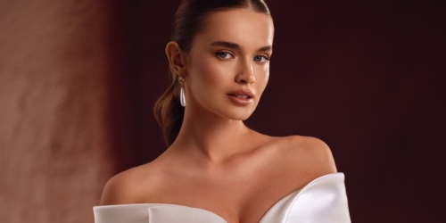 Braut im schulterfreien Satin-Brautkleid Avin von DAMA Couture, mit glatt zurückgenommenen Haaren und einem langen Tropfenohrring.
